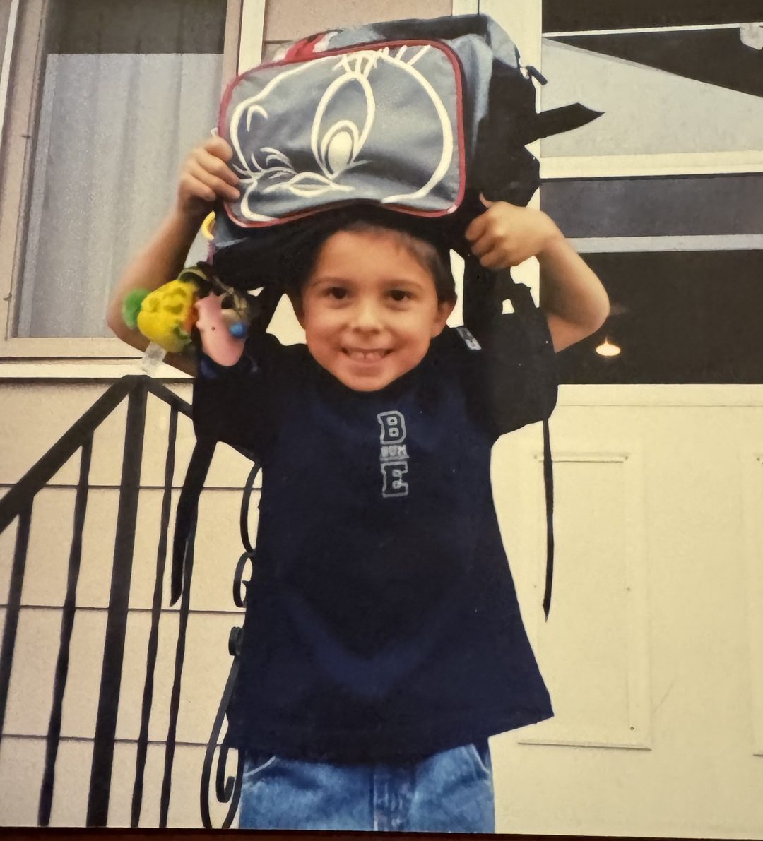 Grade-school John grinning behind an oversized Tweety Bird backpack.