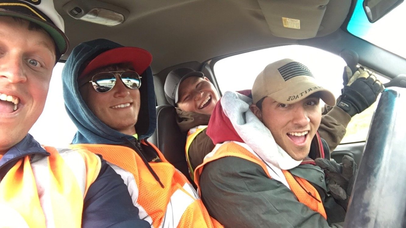 John and three friends laughing in a work truck, all in orange safety vests, on a guardrail crew.
