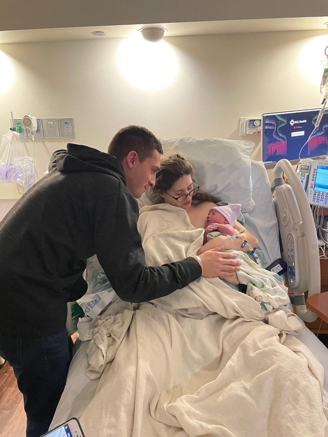 John leaning over Kaylee in a hospital bed as she cradles their newborn son, John V.